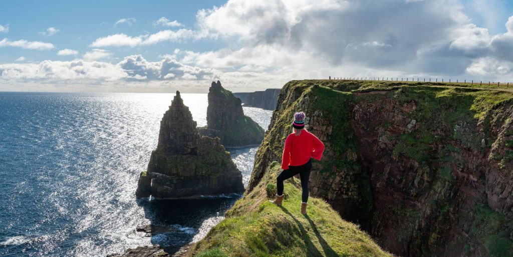A lady standing on a sunny day enjoying a view of the spectacular Duncansby Stacks on the NC500.